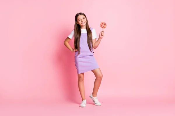 Foto panjang lengkap dari anak gadis positif terus lolipop lezat memakai ungu secara keseluruhan terisolasi atas latar belakang warna pastel — Stok Foto