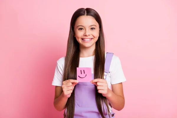 Foto de niña bonita sostiene pegatina con emoticono sonriente aislado sobre fondo de color pastel rosa — Foto de Stock