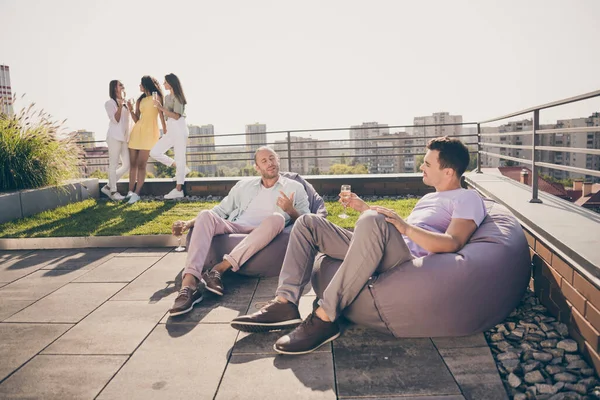 Foto av två unga leende glada gott humör glada män dricka champagne sitta fåtölj prata chatt utanför på taket — Stockfoto