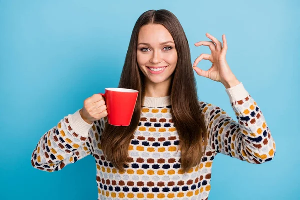 Foto de doce jovem senhora usar camisola ornamento beber café copo vermelho mostrando okey isolado fundo de cor azul — Fotografia de Stock