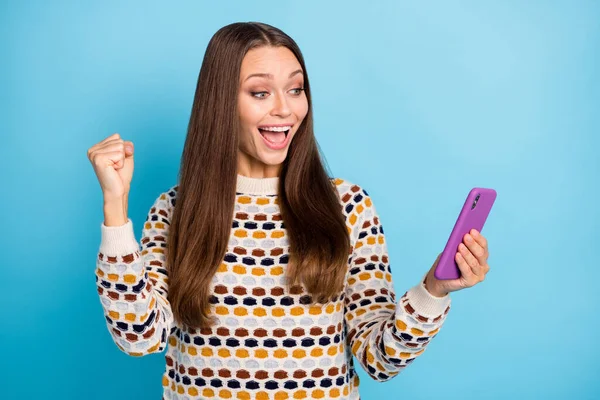 Zdjęcie szczęśliwej młodej kobiety ubrany pullover ozdoba patrząc nowoczesne urządzenie podnoszące pięść odizolowany niebieski kolor tła — Zdjęcie stockowe