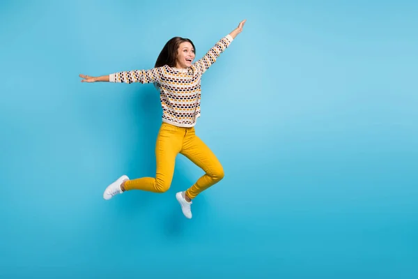 Foto de comprimento total de despreocupado jovem senhora desgaste ornamento suéter pulando mãos braços lados isolado azul cor fundo — Fotografia de Stock