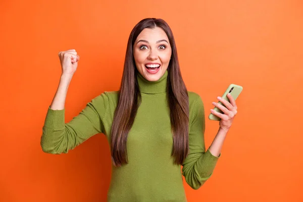 Foto de jovem atraente menina feliz sorriso animado vitória vitória loteria uso smartphone punhos mão isolado sobre cor laranja fundo — Fotografia de Stock