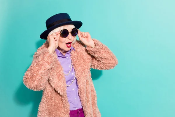 Φωτογραφία από κατάπληκτη ηλικιωμένη κυρία φορούν ρετρό σακάκι headwear χέρια γυαλιά κενό χώρο απομονωμένο φόντο teal χρώμα — Φωτογραφία Αρχείου