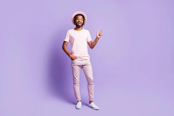 Full size foto di giovane allegro positivo afro uomo ragazzo punto dito in copyspace tenere tasca della mano isolato su sfondo di colore viola — Foto Stock