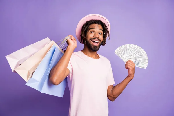 Foto mladého šťastně se usmívá pohledný afro muž muž chlap držet nákupní tašky peníze dolarů izolovaných na fialové barvy pozadí — Stock fotografie