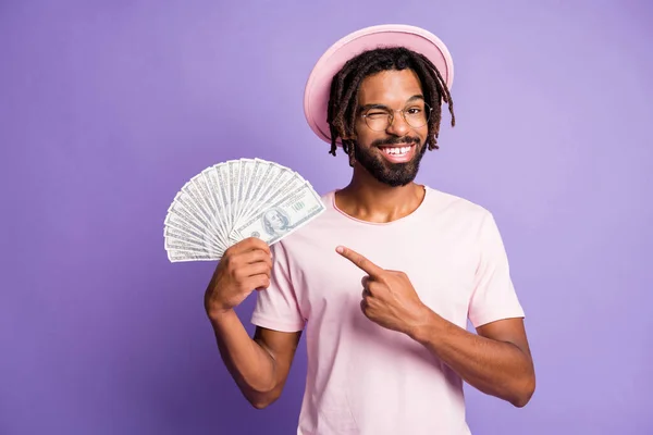 Photo of young handsome african happy smiling man guy wink eye point finger at dollars isolated on violet color background — Stock Photo, Image