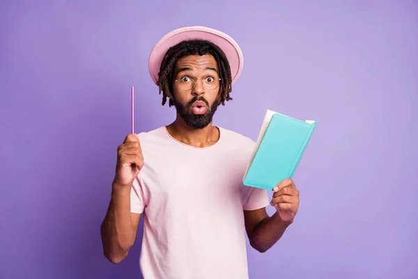 Photo de jeune afro surpris beau homme homme mâle point stylo dans l'espace de copie tenir journal bleu isolé sur fond de couleur violette — Photo