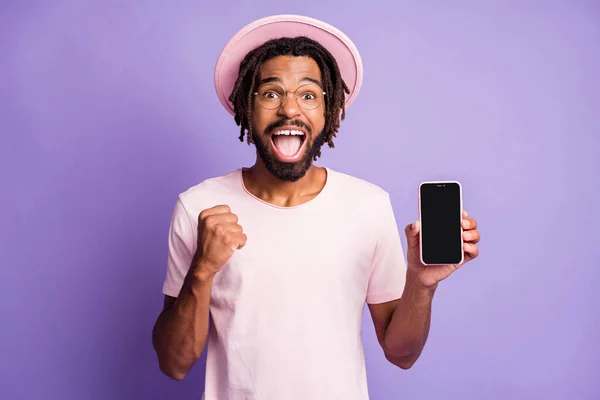 Genç afro yakışıklı adamın fotoğrafı, gülümseyen adam ağzı açık, telefon ekranını göster, yumruğunu menekşe rengi arka planda izole et. — Stok fotoğraf