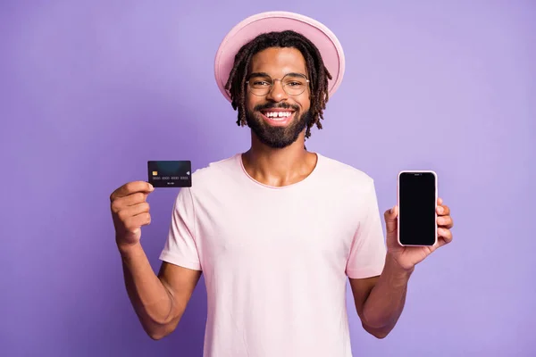 Portrait photo de l'homme en chapeau coiffure élégant tenant téléphone carte de crédit avec copyspace sur écran isolé sur fond violet vif — Photo