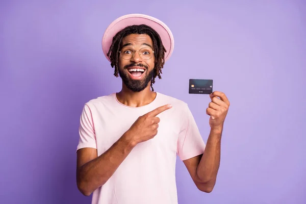 Foto portrét chlapa držícího v jedné ruce ukazující prst na debetní kartě izolované na živém fialovém pozadí — Stock fotografie