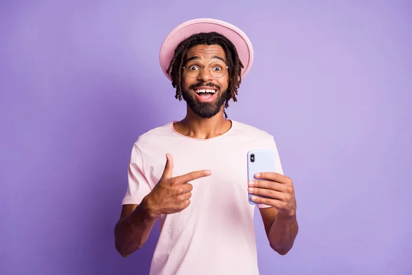 Foto portrét chlapa ukazující prstem na držení telefonu v jedné ruce izolované na živé fialové barevné pozadí — Stock fotografie