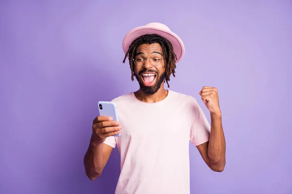 한 손에 핸드폰을 들고 축하하는 분홍색 머리쓰개를 하고 있는 남자의 사진, 선명 한 보라색 배경 위에 고립 — 스톡 사진