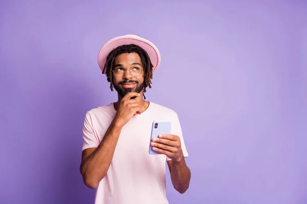 한 손에 핸드폰을 들고 밝은 보라색 배경에 고립 된 수염을 만지고 있는 멋진 핑크 모자를 쓴 왕자의 사진 — 스톡 사진