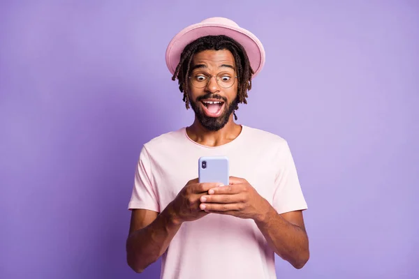 Foto retrato de cara animado em headwear rosa segurando telefone em duas mãos isoladas em fundo colorido violeta vívido — Fotografia de Stock