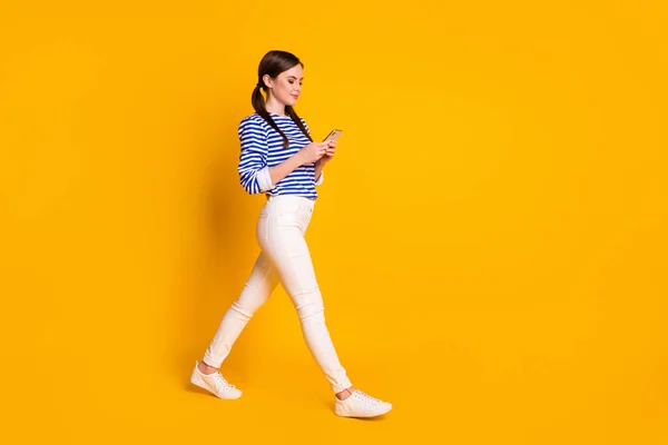 Full size profiel zijkant foto van meisje gaan lopen copyspace gebruik smartphone hebben social media communicatie vriend dragen stijlvolle kleding sneakers geïsoleerde heldere glans kleur achtergrond — Stockfoto