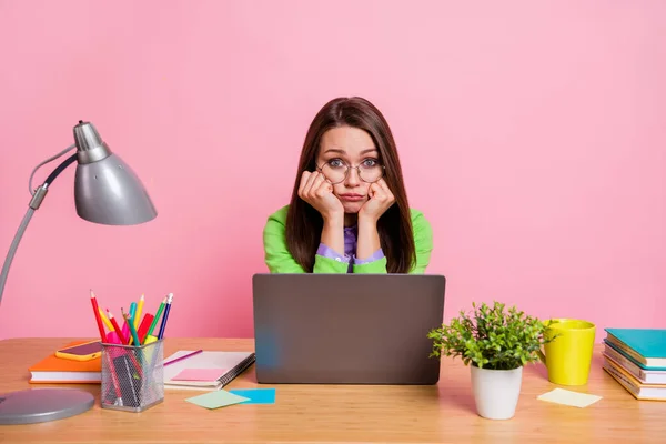 Muchacha molesta sentarse escritorio trabajo portátil tocar puños mejillas pómulos usar camisa verde aislado pastel color fondo —  Fotos de Stock