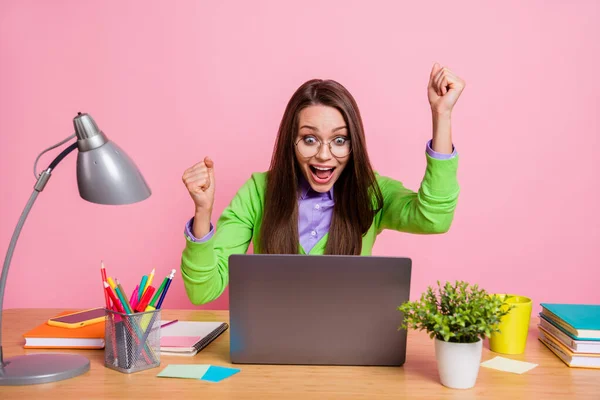 Foto emocionada chica sentarse mesa portátil ganar levantar puños gritar usar camisa verde aislado pastel color fondo —  Fotos de Stock