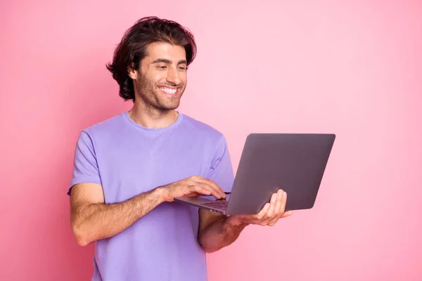 Портрет красивого чоловіка виглядає використовуйте нетбук позитивний програміст одягнений фіолетовим ізольованим на рожевому кольоровому фоні — стокове фото