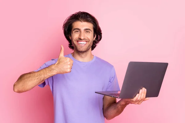 Foto de bonito elegante moderno marrom cabelo jovem segurar laptop polegar-se desgaste camiseta violeta isolado no fundo cor-de-rosa — Fotografia de Stock