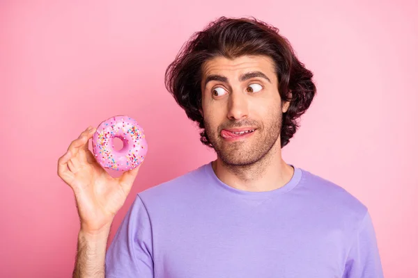 Photo de jeune homme accro affamé regarder tenir beignet lècher lèvre isolé sur fond de couleur rose brillant — Photo