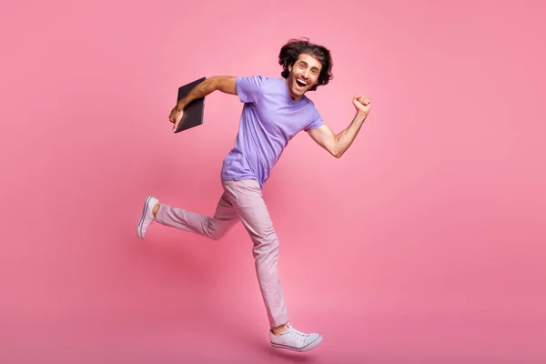 Full size profile side photo of trendy stylish guy jump run sale wear pink pants violet t-shirt hold laptop isolated on pink color background
