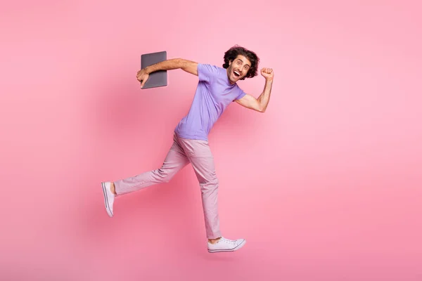 Повний профіль тіла фотографія коричневого волосся модний стильний хлопець тримає ноутбук запустити рожеві штани фіолетові футболки ізольовані на рожевому кольоровому фоні — стокове фото