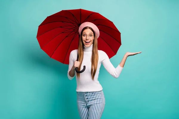 Foto de señora bastante emocionada mantenga gran paraguas rojo mantenga abierto brazo novedad anuncio producto precio bajo oferta desgaste especificaciones boina rosa cuello alto blanco pantalones vaqueros de rayas aislados color verde azulado fondo — Foto de Stock