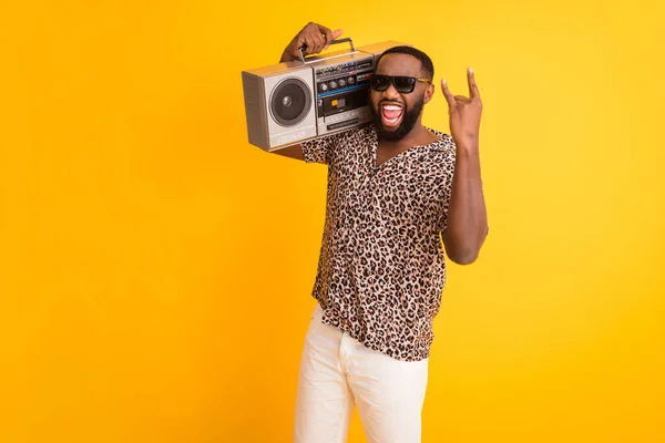 Foto van gekke knappe donkere huid man houden schouder retro tape recorder tonen vinger hoorns rocker ziel dragen shorts luipaard shirt zonnebril geïsoleerde levendige gele achtergrond — Stockfoto