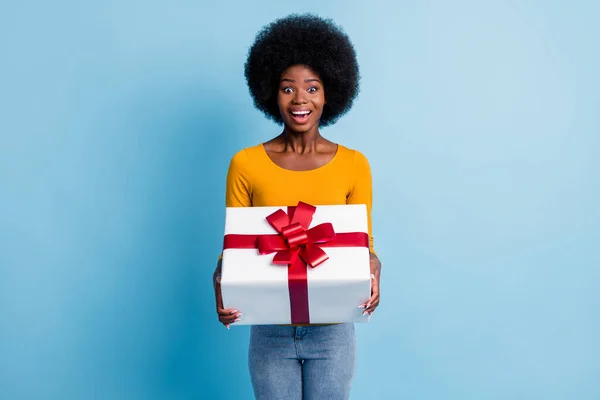 Kırmızı kurdele hediyesiyle sarılı, parlak mavi arka planda saklanmış, gülümseyen siyahi bir kadının fotoğrafı. — Stok fotoğraf