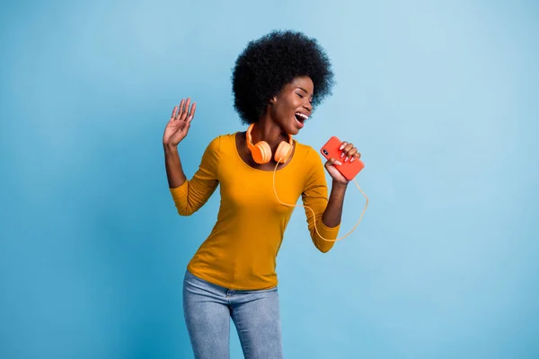 Foto portret van zwart gevild meisje dragen oortelefoons zingen houden smartphone stel je microfoon geïsoleerd op helderblauwe kleur achtergrond — Stockfoto