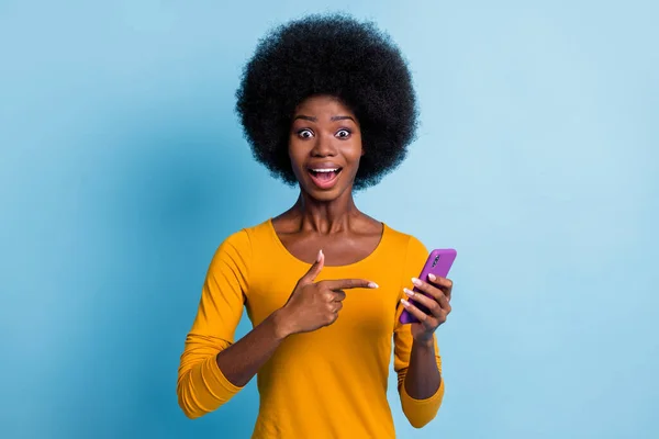 Φωτογραφία πορτρέτο του χαρούμενα μαύρο δέρμα κορίτσι δείχνοντας με το δάχτυλο στο smartphone απομονώνονται σε ζωντανό φόντο μπλε χρώμα — Φωτογραφία Αρχείου