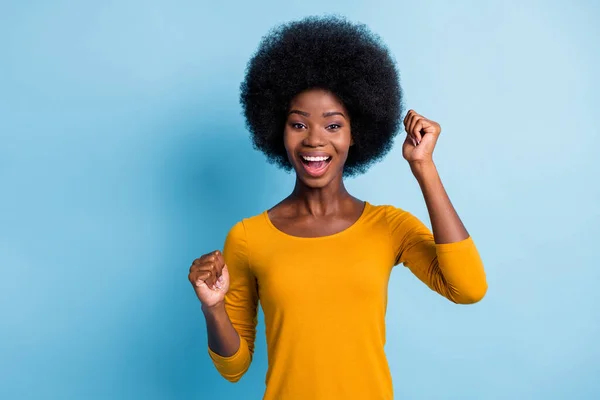 Foto av härlig svart ung flicka volym frisyr höja armarna öppna munnen upphetsad ansikte bära gul skjorta isolerad blå färg bakgrund — Stockfoto