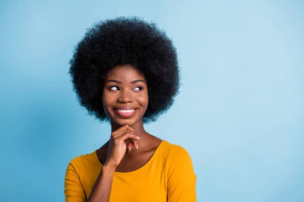 Foto de chica negra pensativa buscar espacio vacío dedo barbilla sonrisa blanca usar camisa amarilla aislado color azul fondo —  Fotos de Stock