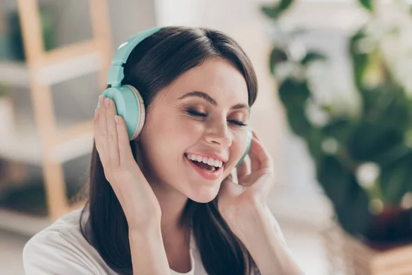 Foto de chica joven positiva escuchar música en auriculares azules inalámbricos usar ropa de estilo casual en casa en interiores — Foto de Stock