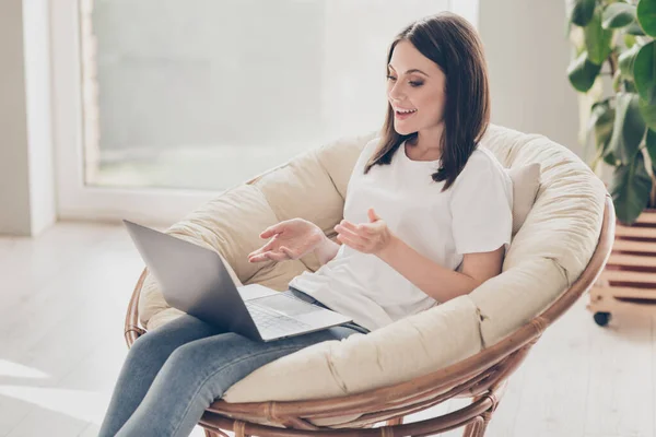 Pozytywny dziewczyna wideo rozmowy na laptop siedzieć wiklinowe krzesło w domu pokój dzienny — Zdjęcie stockowe