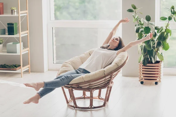 Full length photo of pretty young lady sit wicker armchair stretch arms φορούν casual στυλ ρούχα στο σπίτι — Φωτογραφία Αρχείου