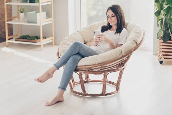 Full size photo of focused girl sit wicker chair comment post on cell phone in house indoors wear casual style clothes — стоковое фото