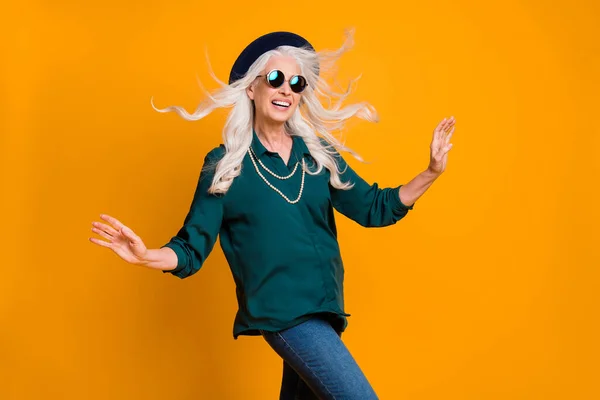 Φωτογραφία από τα όμορφα άσπρα μαλλιά γιαγιά κυρία με τα πόδια δρόμο απολαύσετε ζεστή αύρα εποχής hairdo πτήση φορούν πράσινο πουκάμισο sun specs κολιέ τζιν καπέλο ρετρό απομονωμένο φωτεινό κίτρινο χρώμα φόντο — Φωτογραφία Αρχείου