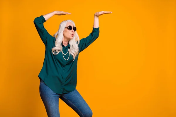 Foto de vovó louco amante da música senhora festa retro sênior olhar fresco dançar estranho jovem se move usar camisa verde sol especificações pérolas colar jeans isolado cor amarela brilhante fundo — Fotografia de Stock