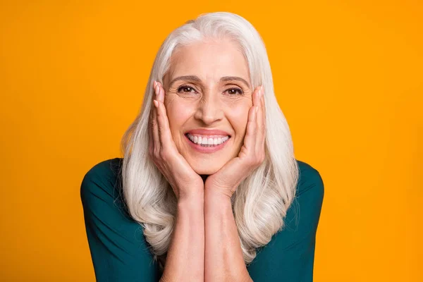 Foto de primer plano de increíble alegre de pelo blanco abuela anciana dentadura sonriente brazos llenos de alegría en las mejillas afectuoso desgaste camisa verde aislado vibrante fondo amarillo —  Fotos de Stock