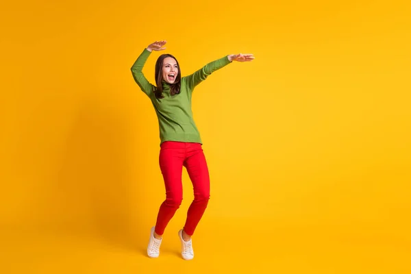 Взгляд в полный рост на привлекательную жизнерадостную худенькую девушку, прыгающую, весело танцующую на ярко-желтом фоне — стоковое фото
