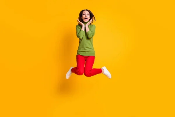Encantadora señora loca saltar encima de las mejillas de los brazos usar casual jersey verde zapatillas pantalones rojos aislados de color amarillo fondo —  Fotos de Stock