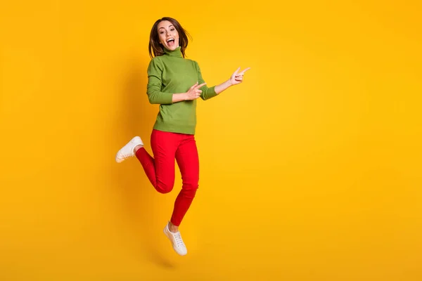 Pretty lady jump up directing fingers empty space wear pullover sneakers trousers isolated yellow color background — Stock Photo, Image