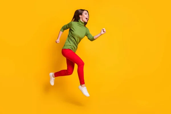 女士兴奋地跳起来，穿着休闲的绿色套头鞋，红裤孤立的黄底色 — 图库照片