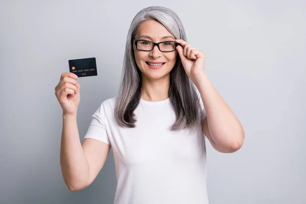 Foto di pensionato nonna tenere carta di debito dita specs indossare occhiali bianco t-shirt isolato colore grigio sfondo — Foto Stock