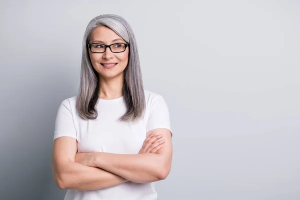 Foto di matura vecchia signora sorriso dentato braccia piegate sguardo vuoto spazio usura specifiche bianco t-shirt isolato colore grigio sfondo — Foto Stock