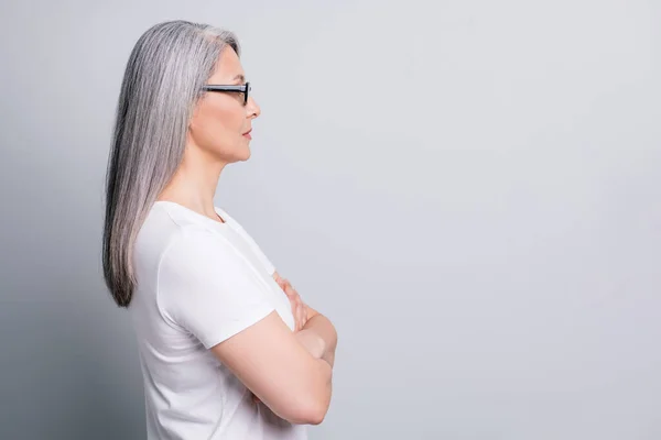 Profiel foto van gepensioneerde vrouw kijken lege ruimte gekruiste armen dragen bril wit t-shirt geïsoleerde grijze kleur achtergrond — Stockfoto