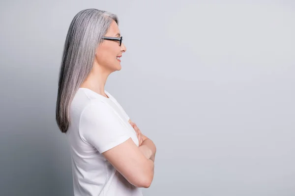 Profiel foto van vrolijke oude vrouw kijken lege ruimte gekruiste handen dragen bril wit t-shirt geïsoleerde grijze kleur achtergrond — Stockfoto