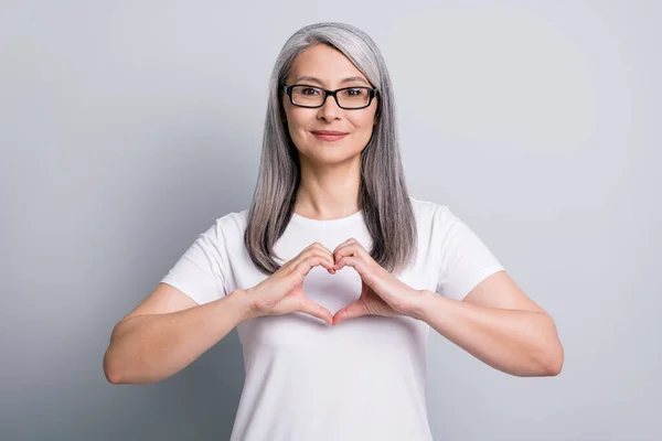Foto de senhora madura pacífica apresentando forma de coração desgaste óculos branco t-shirt isolado cinza cor fundo — Fotografia de Stock